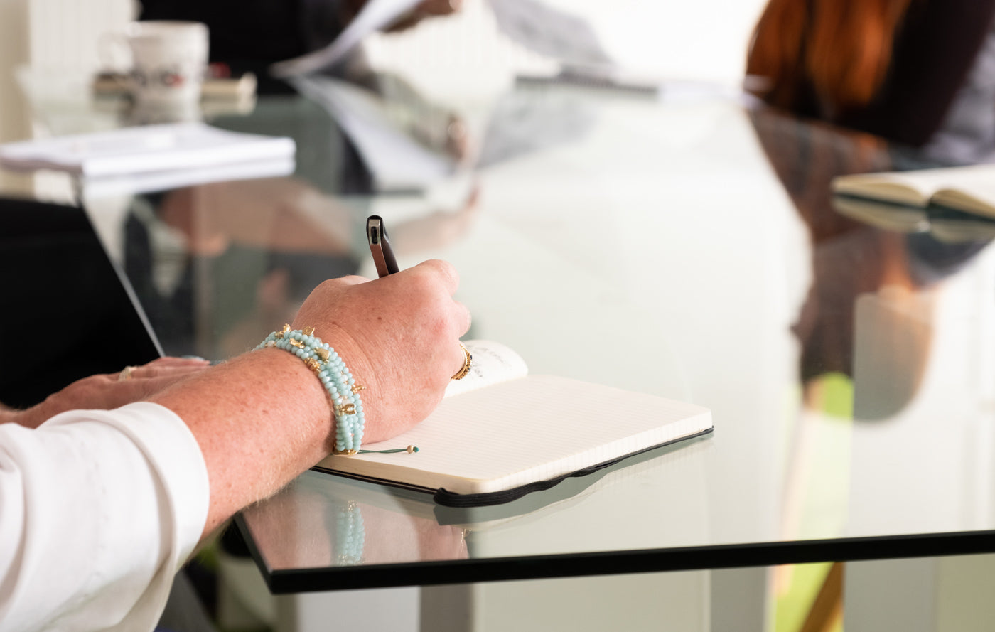 Ladies_bangled_hand_writing_in_notepad_on_glass_boardroom_table.jpg