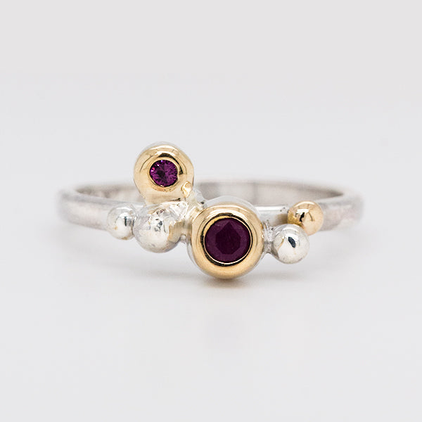 This is an image of a sterling silver ring with yellow gold and two ruby gems.  One ruby gem is larger than the other.