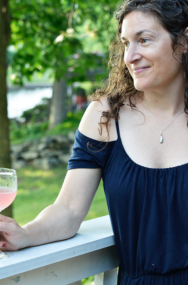 Julie wearing silver Strength droplet peridot necklace with glass of rose wine outside