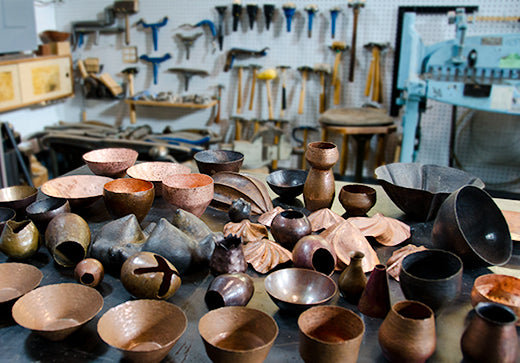 table full of hammered copper and brass sculptural vessels in Catherine Grisez metalsmithing studio