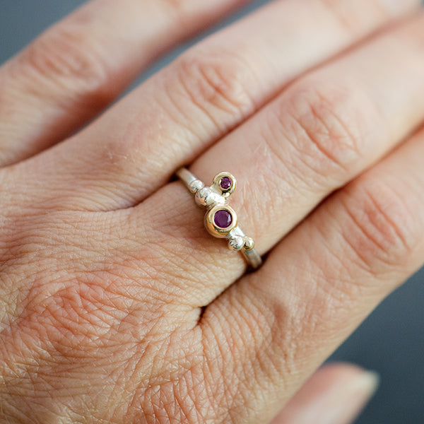 This an image on the hand of a woman she is wearing a sterling silver ring with yellow gold and two rubies.  One ruby is larger than the other. 