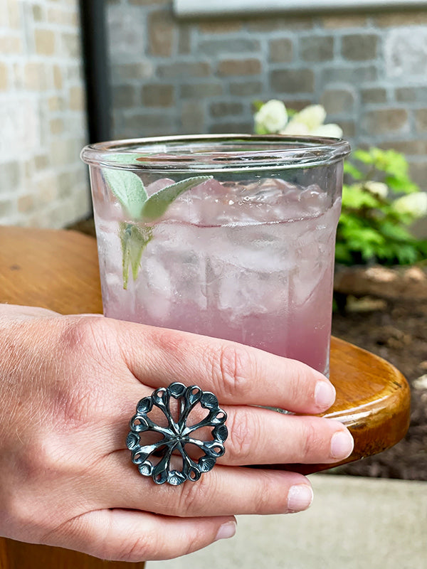 darkened silver sea flower power ring holding pink blueberry cocktail outside
