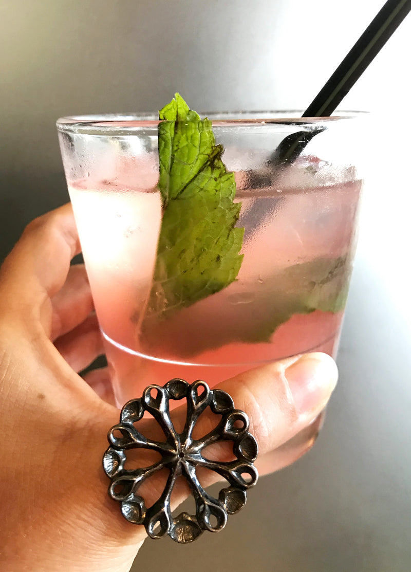 big flower power ring on thumb and glass of pink cocktail with mint