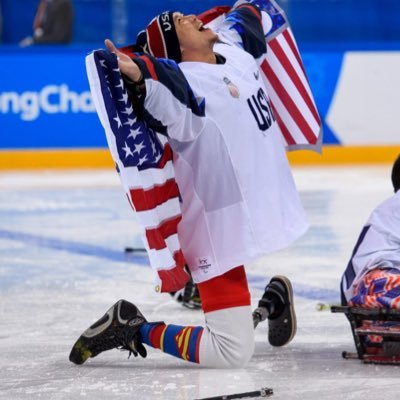 Jen Lee on the ice celebrating sled hockey win, holding American flag overhead 