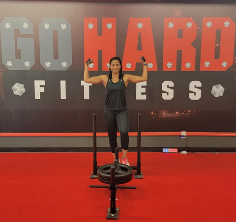 woman stands in gym with arms raised looking strong and powerful