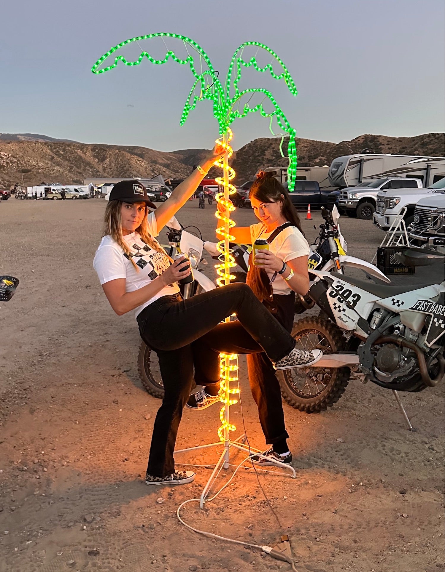 Two girls hanging next to a light-up palm tree at a women's dirt bike event. Babes in the Dirt 2023.