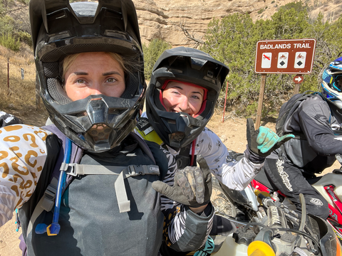 Two woman in dirt bike gear standing in front of a trail sign in Gorman