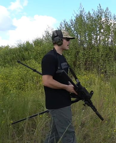 Chris French carries a rifle attached to a tripod