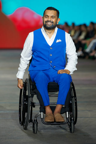 A dark haired man in a wheelchair wearing an electric blue waistcoat and pants with a white shirt