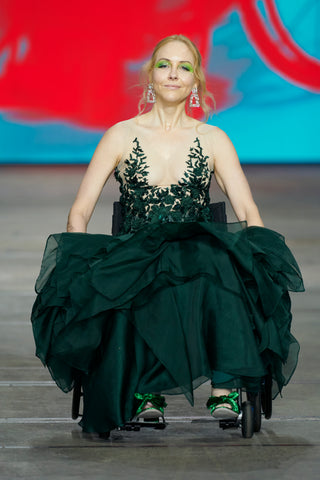 A blonde haired woman in a wheelchair wearing an emerald green ruffled formal dress