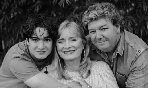 A black and white image of Carol (centre) being hugged by her son D'arcy (left) and husband Rob (right.)