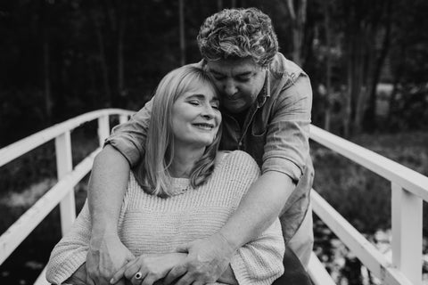 A black and white photo of Carol with her eyes closed being hugged by her husband Rob.