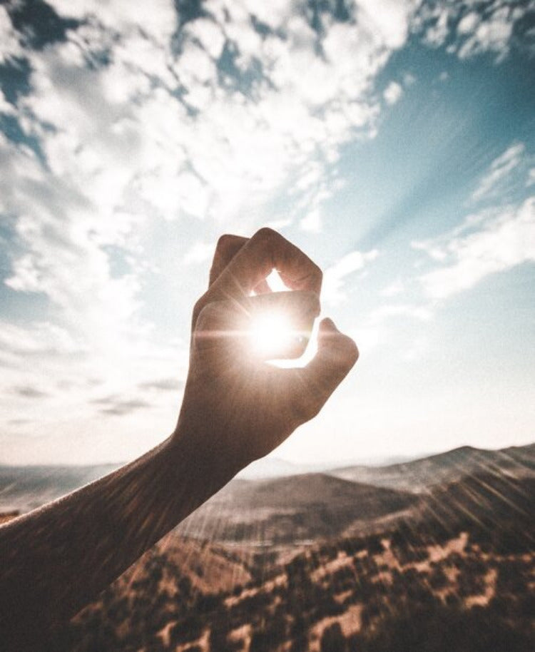 Hand forms a hole through which the sun shines Sky in the background