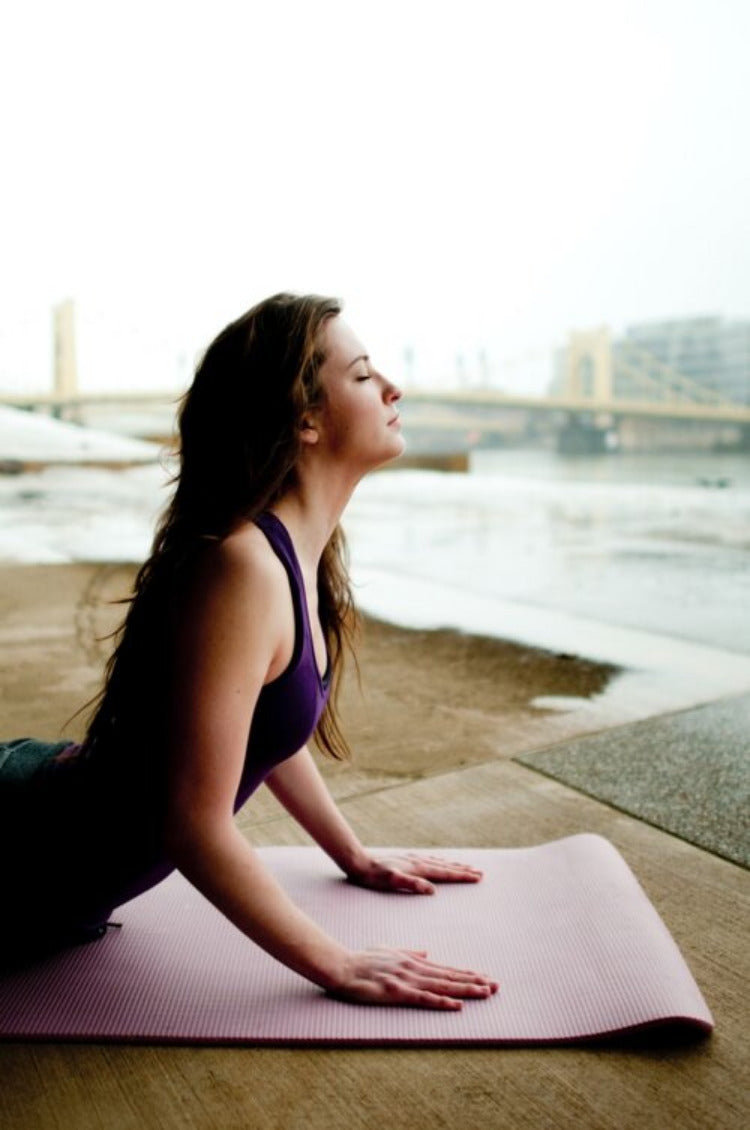 Woman doing yoga on yoga mat stones nature blurred in background