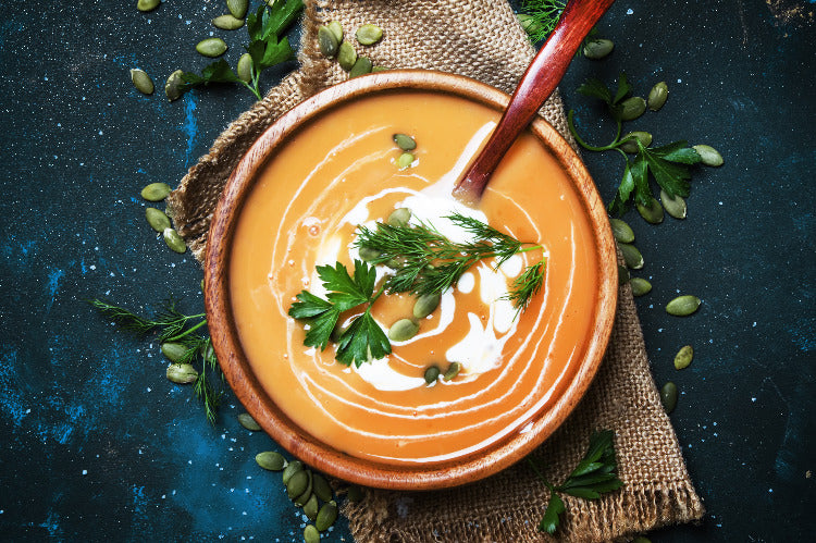 Soup in a wooden bowl, wooden spoon, linen cloth, herbs, blue worktop