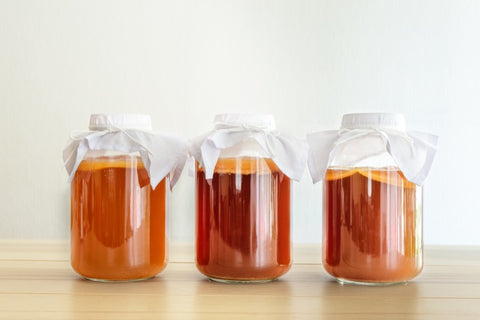 Trois grands pots en verre avec kombucha recouverts de tissu en coton