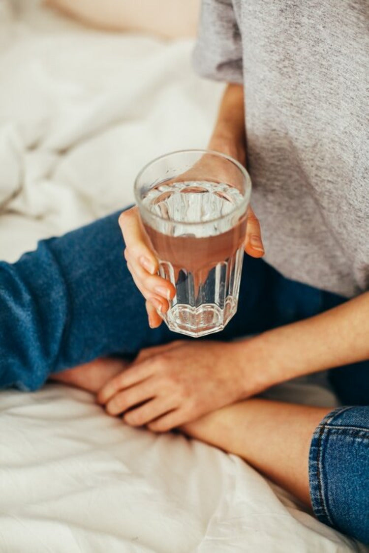 Detail Woman holding a large water glass with water sits on the floor