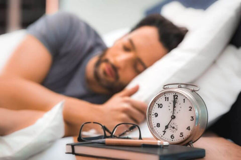 Homem deitado na cama com despertador e óculos ao lado