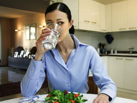 Mulher bebendo água enquanto come