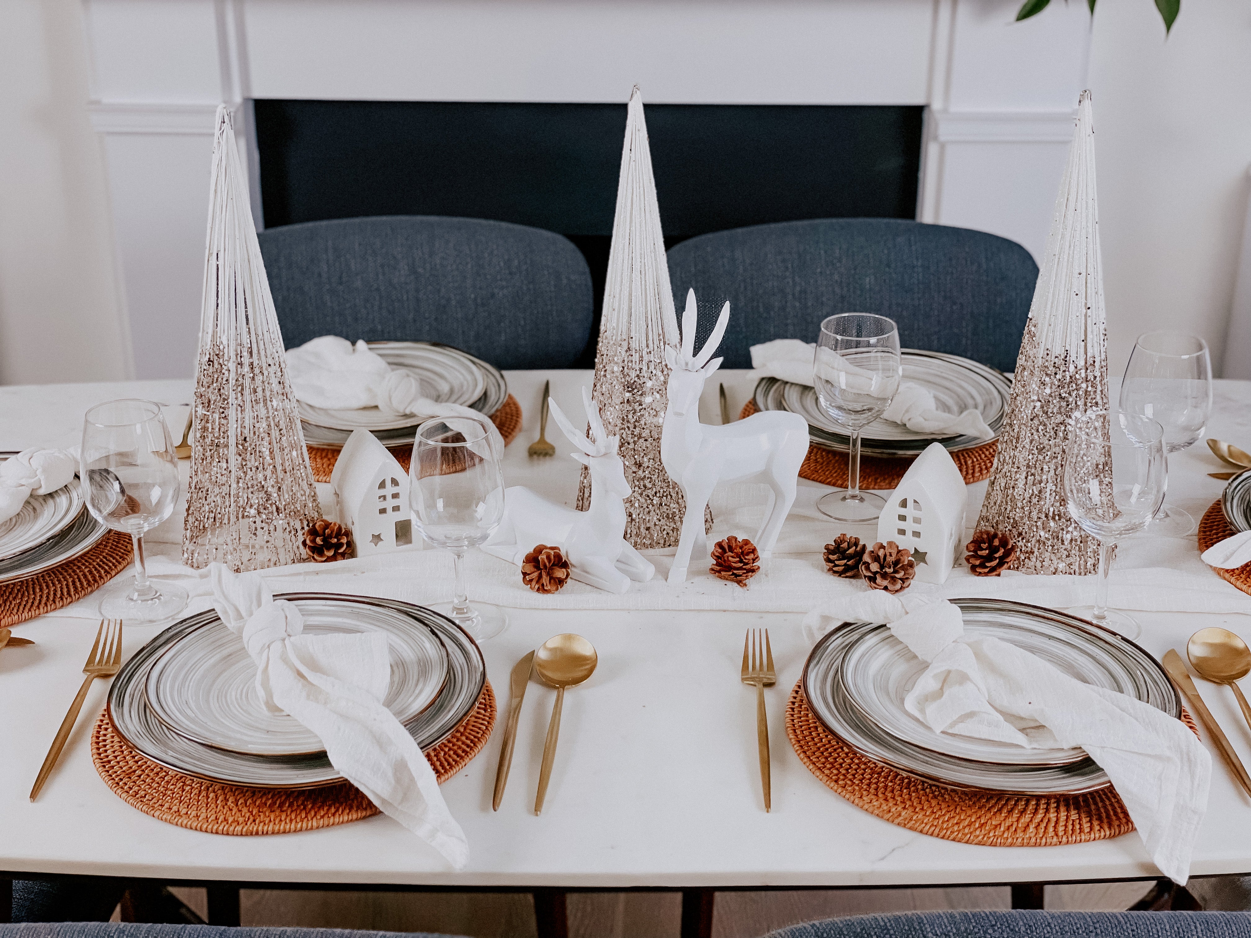 What a Host Home Decor: Christmas Tablescape With Geometric Decorative Christmas Deers, Scandi Houses, Rattan Placemats, White and Gold Christmas Table Pine Trees, Porcelain Plates Set Tableware, Gold Cutlery Stainless Steel Set and Rustic Cotton Gauze Table Textiles