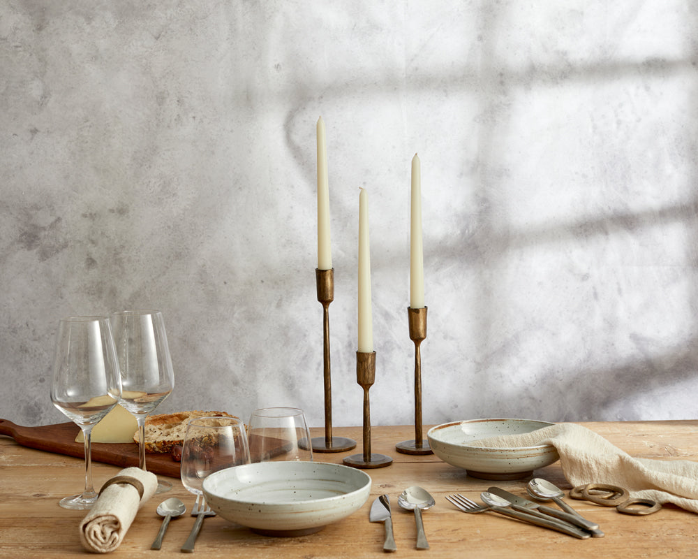What a Host Home rustic table setting with gold brass candle holders, rustic stainless steel cutlery sets, cotton napkins and brass rustic napkin rings