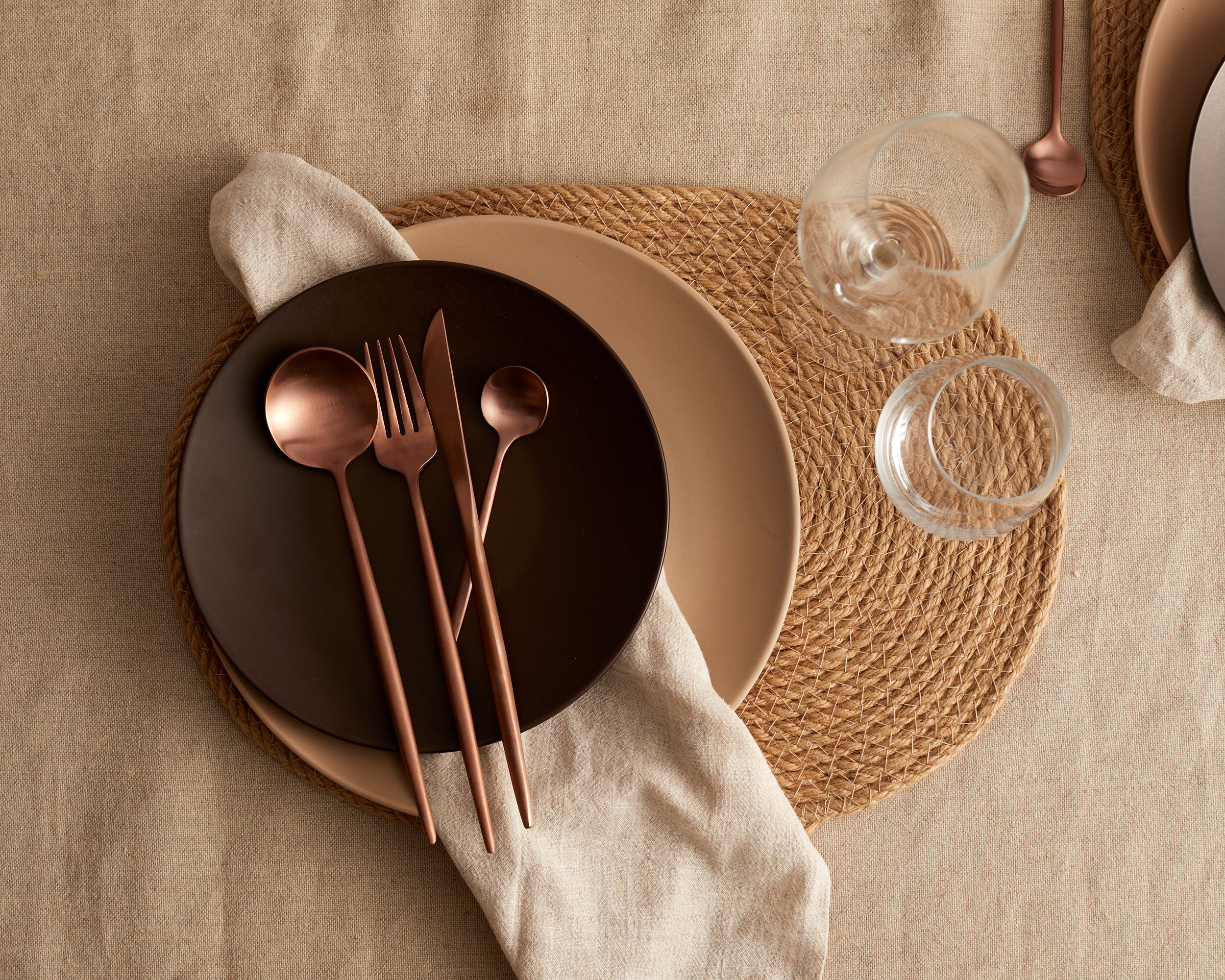 Jute Oval Placemat, round ceramic plates set, copper rose gold cutlery set in stainless steel and linen table napkins from What a Host Home