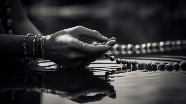 A black and white photo of an individual contemplating their reflection in water, subtly featuring a piece of jewelry, symbolizing the origins of personal decoration.