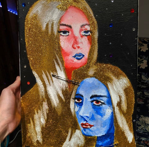 The Galactic Twins: Blue and Red figures with gold glitter hair and painted highlights. This piece has a Black background with jewels like stars in the sky. Mixed media piece was a great gift.