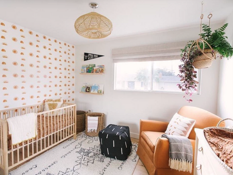 Sun lit contemporary nursery with wooden cot, arm chair and hanging plants.