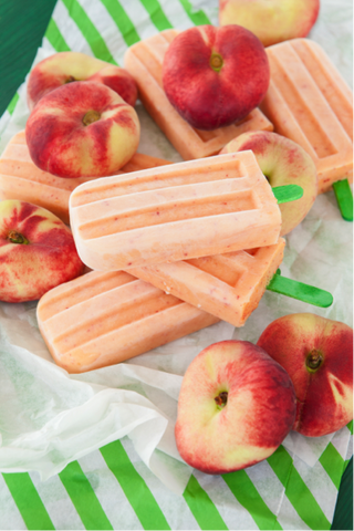 Peach Popsicles on talbe surrounded by peaches