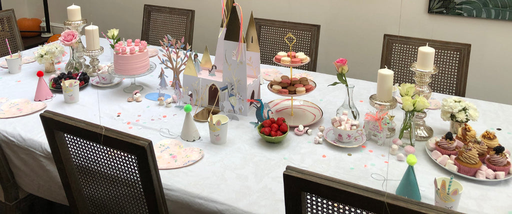 The table’s set for a tea-party with a birthday cake, fairy cakes and a cardboard castle.