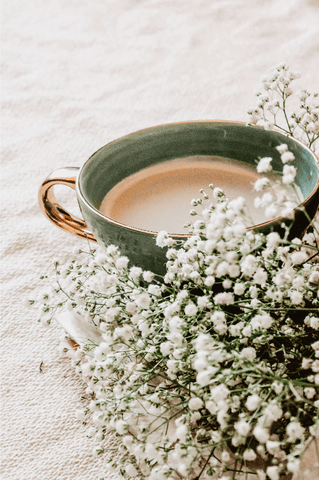 Café en taza sobre la cama y ramo de flores relax