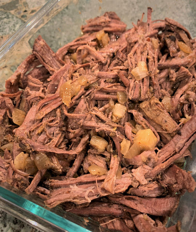 shredded beef brisket with cooked onions in a glass serving dish