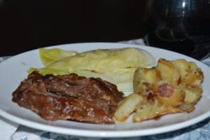 white plate with cooked beef brisket, roasted potatoes, and steamed cabbage