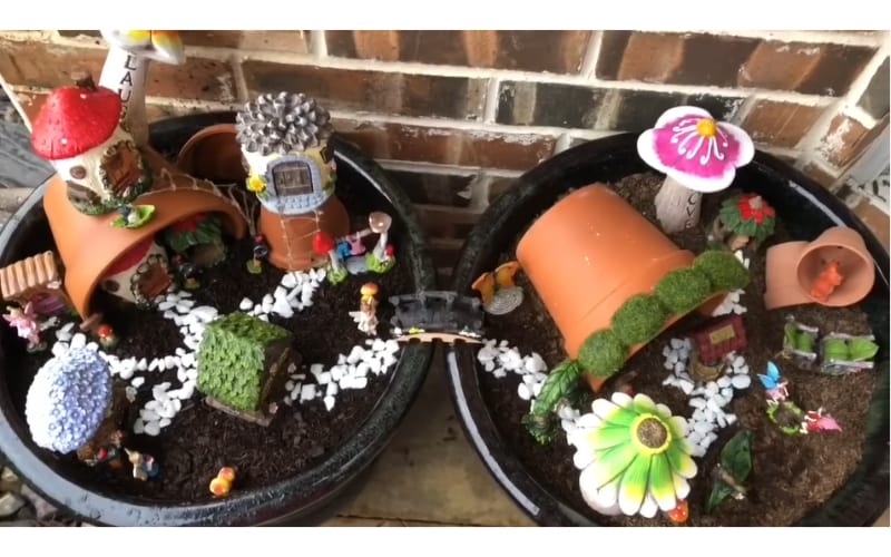 a fairy garden with lots of accessories from terracotta planters, pebbles, houses, and fairies