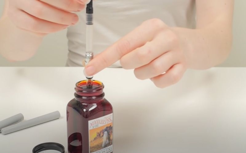 a woman dipping the pen in the bottle of  ink
