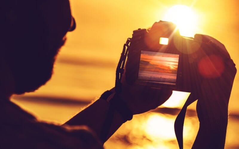 A man taking photographs of the sunset using a digital camera