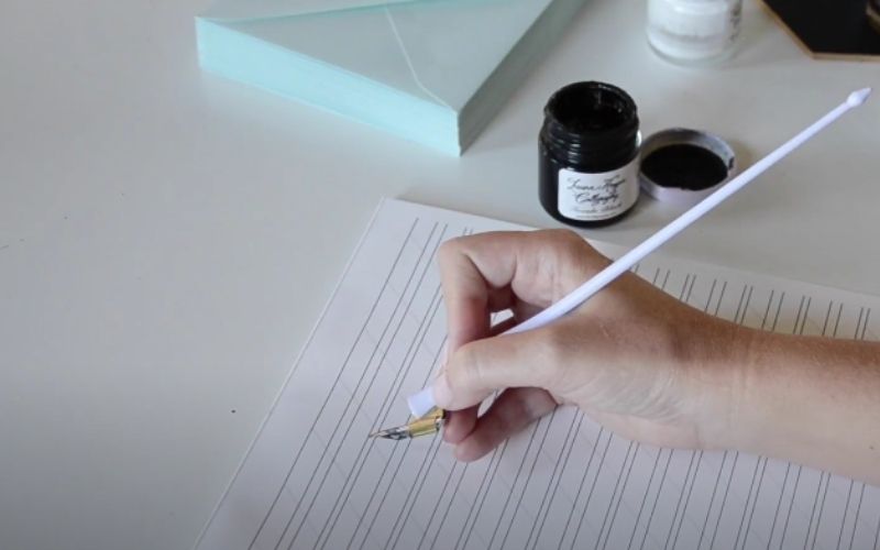 a woman holding a calligraphy pen on the tracing paper