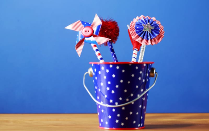 A festive bucket filled with pinwheels, a pompom, and other crafts that younger kids can make