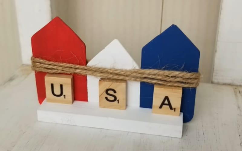 a row of a wooden outline of houses with the Scrabble letters U, S, and A glued to it