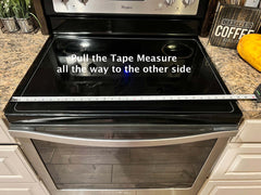 How to measure a stove top cover, noodle board? Picture showing a tape measure pulled all the way across the stove top.
