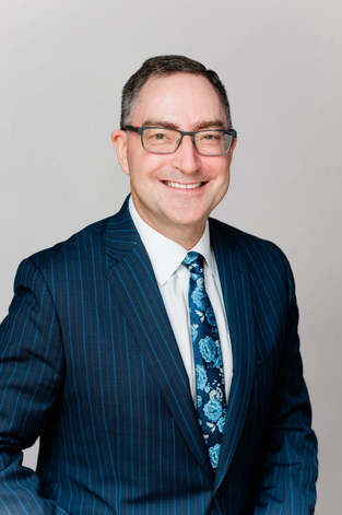 A man in a suit smiling and ready for a professional headshot.