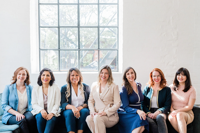 Group of nine professional women sitting and posing for headshots. Each woman presents a confident and professional demeanor in this group portrait.