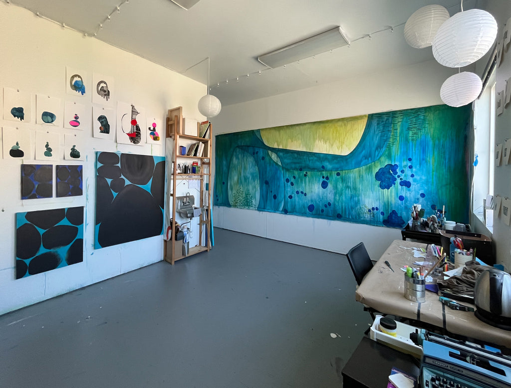 Wide view of studio with large blue painting on right, smaller pieces on left