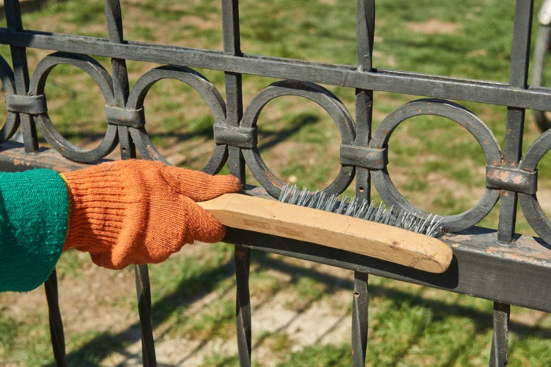 Une personne enlève la rouille de la clôture avec une brosse