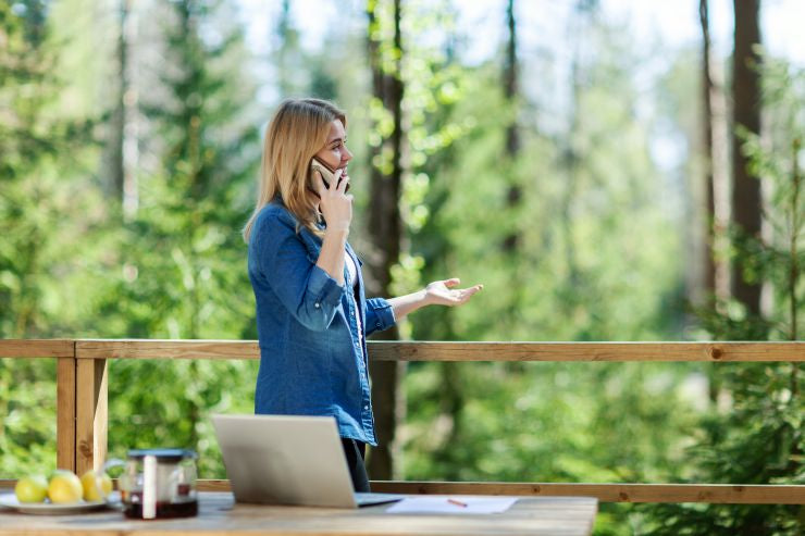 Une femme se tient à la balustrade du balcon en bois et parle au téléphone