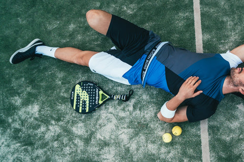 male person lying down in field beside tennis racket and tennis ball