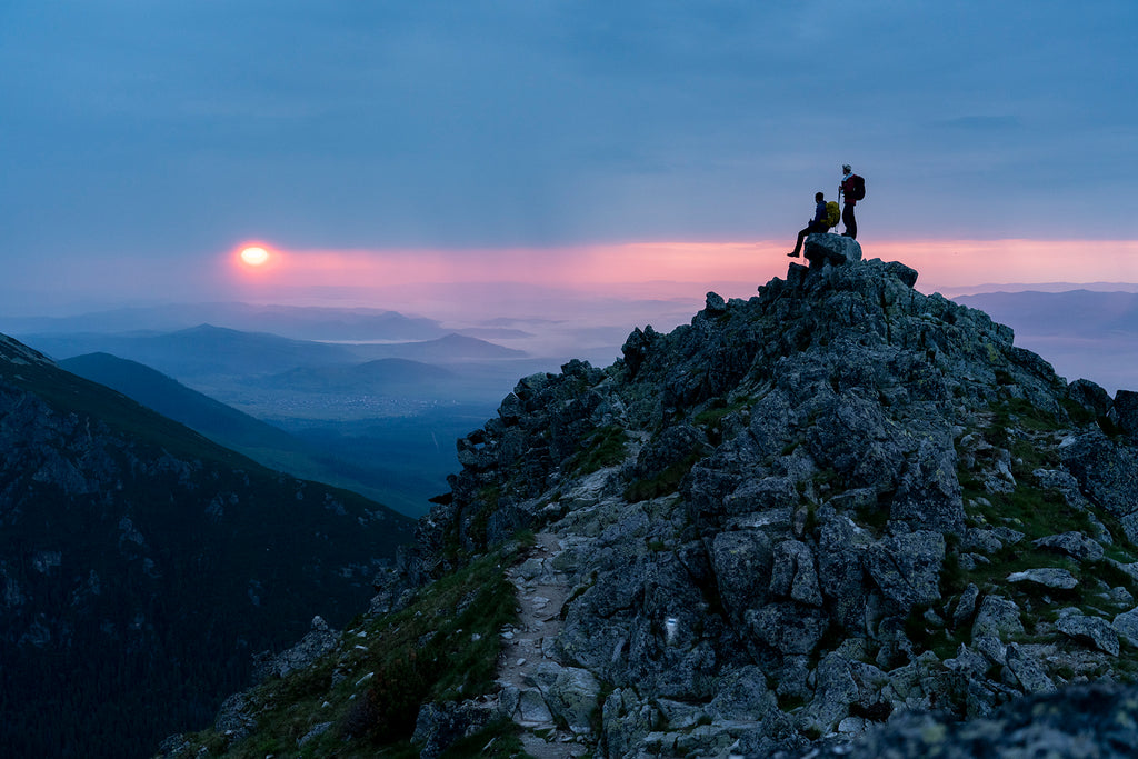 Two trekkers on a mountain watching the sunset