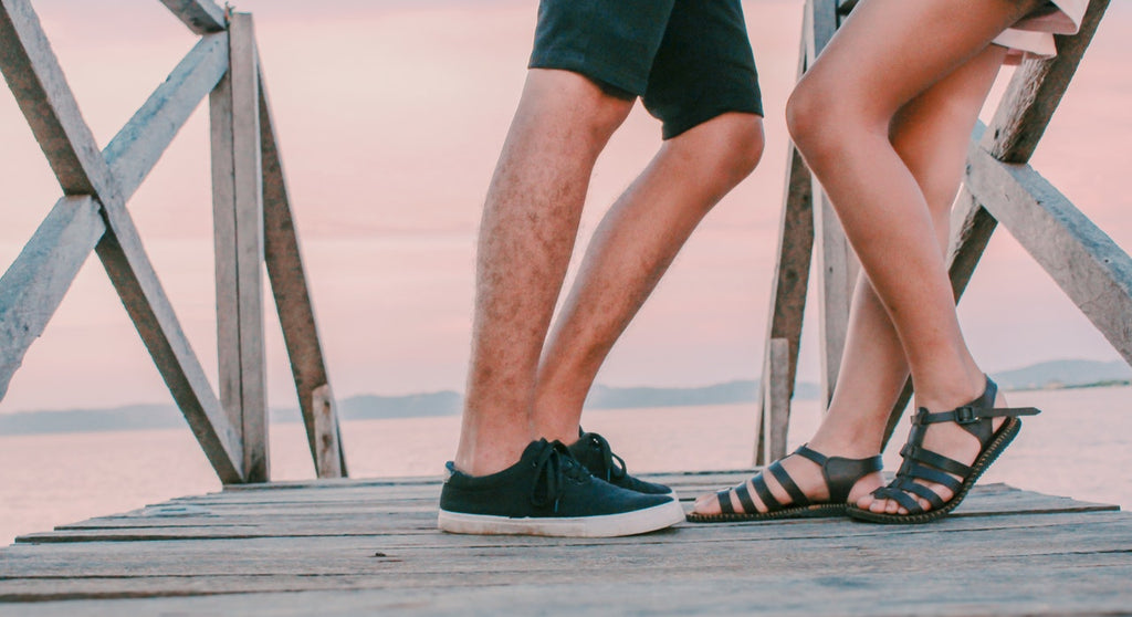 Man wearing trainers and woman wearing sandals, stood opposite each other on a mini pier. 