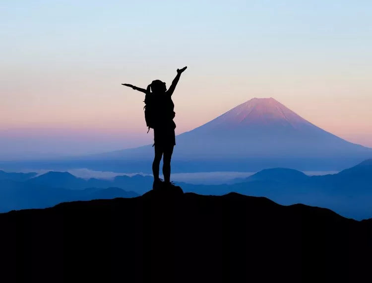 Woman stood at top of a mountain at sunset. 